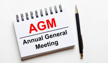 Hafif bir arkaplanda, AGM Yıllık Genel Kurul ve bir kalem içeren beyaz bir defter.