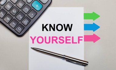 Açık gri bir arkaplanda, bir hesap makinesi, kendinizi tanıyın yazılı beyaz bir sayfa, bir kalem ve parlak renkli çıkartmalar. Yukarıdan görüntüle