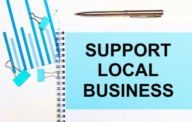 Açık arkaplanda - açık mavi diyagramlar, ataçlar ve metin SUPPORT LOCAL BUSINESS ile bir sayfa kağıt. Yukarıdan bak. İş konsepti