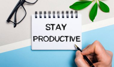 Gri-mavi arka planda, gözlüklerin yanında ve bir bitkinin yeşil yaprağında, bir adam bir kağıt parçasına KALDIRMA YÖNETMENLİK yazısını yazar. Düz yatıyordu. Yukarıdan görüntüle.