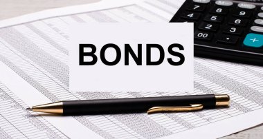 Masaüstü raporlar, hesap makinesi, kalem ve BONDS yazılı beyaz kart içerir. İş konsepti