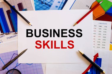 BUSINESS SKILLS kelimeleri renkli grafikler, kalemler ve kalemlerin yanında beyaz bir arkaplanda yazılmıştır. İş konsepti