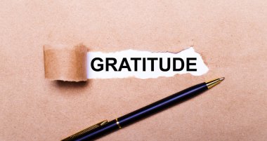 Yırtık Kraft kağıdı, beyaz arkaplan ve GRATITUDE metni. Yakınlarda siyah bir kol var. Yukarıdan görüntüle