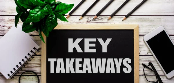 TAKEAWAYS siyah tahtaya, telefonun, not defterinin, gözlüklerin, kalemlerin ve yeşil bitkinin yanında beyazla yazılmıştır..
