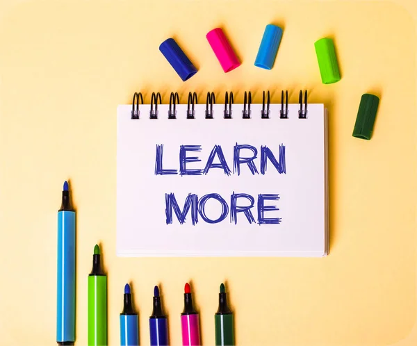 Çok renkli kalemlerin yanında bej bir arkaplan üzerine beyaz bir not defterine Learn More yazıldı.