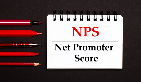 A white notepad with the text NPS Net Promoter Score, written on a white notepad next to red pens, pencils and markers on a black background.