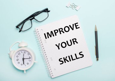 Açık mavi bir arka planda siyah gözlük ve kalem, beyaz bir çalar saat, beyaz ataçlar ve üzerinde 