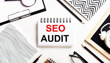 Bir ışık masasında defterler, bir büyüteç, bir çalar saat, bir gözlük ve bir kalem vardır. Ortasında da SEO AUDIT yazılı bir defter var.