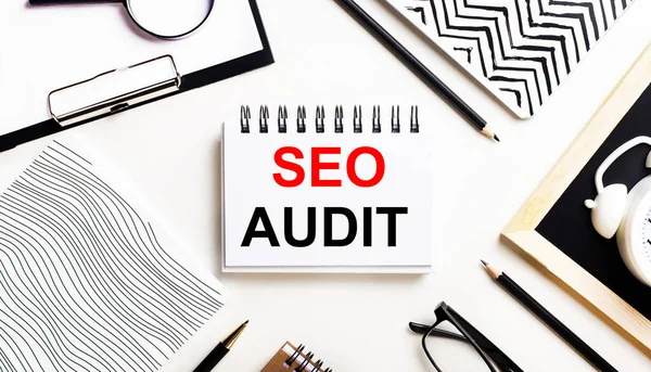 Bir ışık masasında defterler, bir büyüteç, bir çalar saat, bir gözlük ve bir kalem vardır. Ortasında da SEO AUDIT yazılı bir defter var.