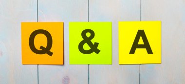 Açık mavi ahşap bir arka planda Q, Sorular ve Cevaplar yazılı üç renkli etiket.