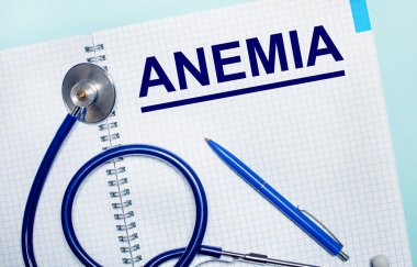 Açık mavi arka planda, üzerinde anemi, mavi kalemi ve steteskopu olan açık bir defter. Yukarıdan bak. Tıbbi konsept