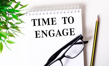 Bağlanma zamanı beyaz bir defterde, siyah çerçeveli bir kalem ve yeşil bir bitkinin yanında yazılır..