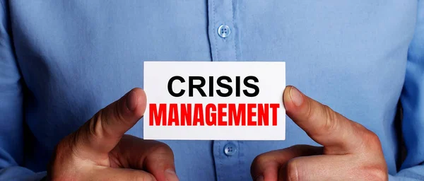 The words CRISIS MANAGEMENT is written on a white business card in a man's hands. Business concept