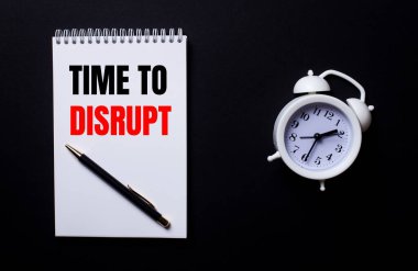 DISRUPT zamanı beyaz bir not defterine siyah bir arkaplanda beyaz bir çalar saatin yanında yazılır..