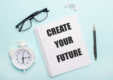 On a light blue background lie black glasses and a pen, a white alarm clock, white paper clips and a notebook with the words CREATE YOUR FUTURE. Business concept