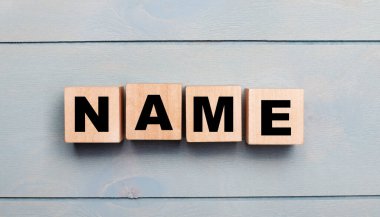 Wooden cubes with the text NAME on a light blue wooden background.