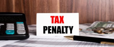 On a wooden background lies pen with calculator and white card with words TAX PENALTY