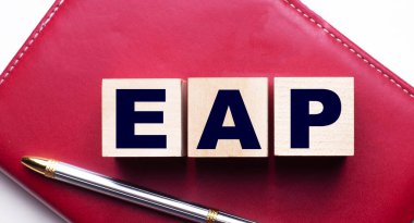 Kalemin yanındaki bordo bir defterin üzerinde duran tahta küplerden oluşan EAP Personel Yardım Programı. İş konsepti