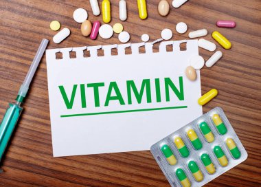 Tahta bir masaya, şırıngaya, haplara ve üzerinde VITAMIN yazan bir kağıt parçasına. Tıbbi konsept