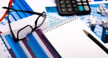 Belge ve çizelgelerin arka planına karşı - defterli bir kalem, bir hesap makinesi ve siyah çerçeveli gözlük. İş konsepti. İş yeri kapanıyor.