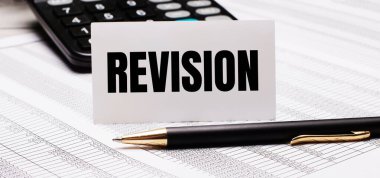 Masanın üzerinde raporlar, bir kalem, bir hesap makinesi ve üzerinde REVISION yazan beyaz bir kart var. Odaklanmayın