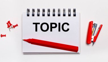 Hafif bir arkaplanda, kırmızı bir kalem, kırmızı bir zımba, kırmızı ataç ve TOPIC yazılı bir defter.