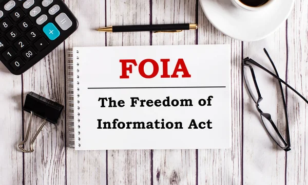 FOIA Bilgi Özgürlüğü Yasası bir hesap makinesinin, kahvenin, bardakların ve kalemin yanında beyaz bir not defterine yazılır. İş konsepti