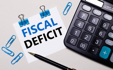 Hafif bir arkaplanda, bir hesap makinesi, bir kalem, mavi ataç ve FISCAL DEFICIT yazılı bir kağıt. Yukarıdan görüntüle