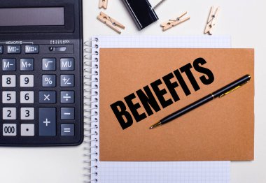 Masaüstünde bir hesap makinesi, bir kalem ve mandallar var. Yanında da BENEFITS metni olan bir defter. İş konsepti. Yukarıdan görüntüle