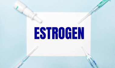 Açık mavi arka planda, şırıngalar, ilaç şişesi, ampul ve ESTROGEN yazılı beyaz bir kağıt. Tıbbi konsept.