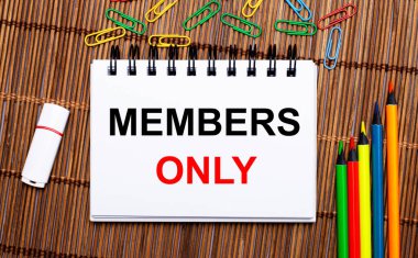 Ahşap bir masada, çok renkli kalemler, ataçlar, beyaz bir flaş bellek ve içinde sadece Üyeler olan bir defter. Düz yatıyordu