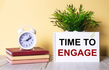 Bağlanma Zamanı, yeşil bir bitki ve renkli günlüklerin üzerinde duran beyaz alarmlı saatin yanındaki defterde yazılıdır..