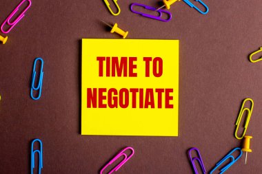 TIMR to NEGOTIATE kelimeleri kırmızı ile yazılmıştır. Kahverengi arkaplandaki sarı çıkartma ile çok renkli ataçların yanındadır..