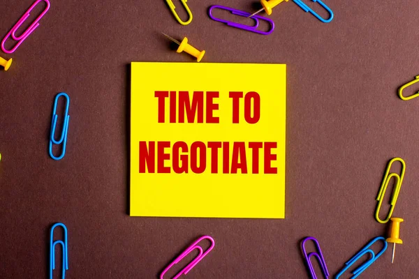 Negotiate的英文 Timr Negotiate 是用红色写在黄色贴纸上的 贴在彩色回形针旁边的褐色背景上 — 图库照片