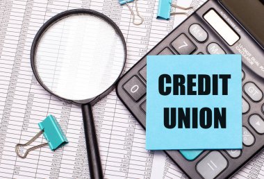 Masada raporlar, bir büyüteç, bir hesap makinesi ve üzerinde CREDIT UNION yazan mavi bir not etiketi var. İş konsepti
