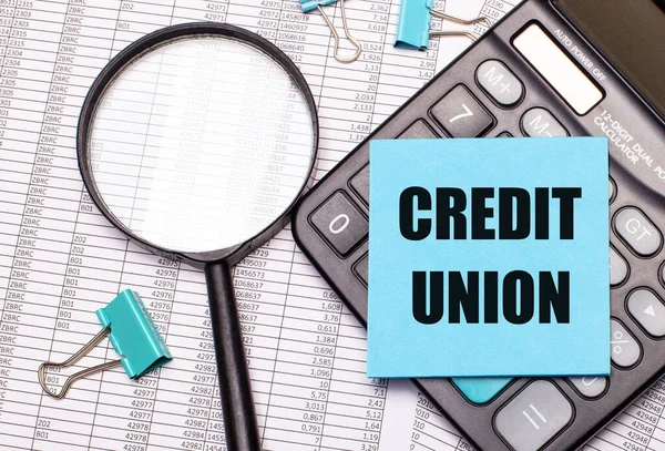 Masada raporlar, bir büyüteç, bir hesap makinesi ve üzerinde CREDIT UNION yazan mavi bir not etiketi var. İş konsepti