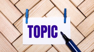 Ahşap bir arka planda mavi mandallarda TOPIC yazılı beyaz bir kart ve mavi bir işaret var. Yukarıdan görüntüle