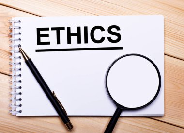 Hafif ahşap bir arka planda bir kalem, bir büyüteç ve ETHICS yazılı bir defter uzanıyor.