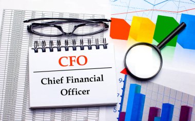 On the desktop are glasses, a magnifying glass, color charts and a white notebook with the text CFO Chief Financial Officer. Business concept. View from above