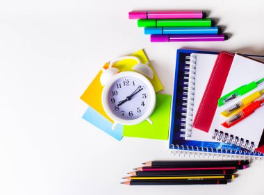 Hafif bir arka planda, parlak renkli bir kırtasiye ve beyaz bir çalar saat. Kopyalama alanı olan düz