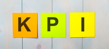 Three colored stickers with the text KPI on a light blue wooden background