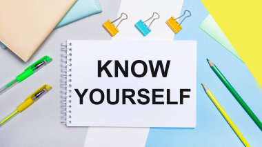 On a gray and blue background are stationery of yellow-green color, a notebook with the text KNOW YOURSELF. Flat lay.