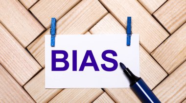 On a wooden background, a white card with the text BIAS on blue clothespins and a blue marker. View from above