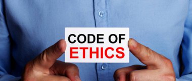 The words CODE OG ETHICS is written on a white business card in a man's hands. Business concept