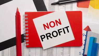 On the desktop are reports, charts, a red pen, a black marker, a red notepad and a white sheet of paper with the text NON PROFIT. Business concept