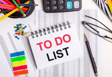 Masanın üzerinde raporlar, hesap makinesi, renkli kalemler ve çıkartmalar, bir kalem ve bir defter var.