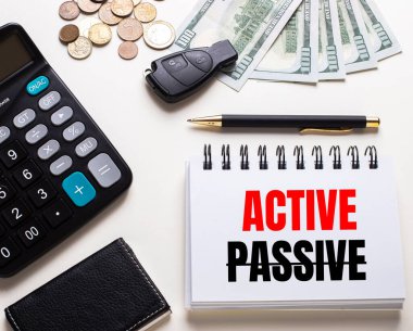 Beyaz bir masada hesap makinesi, araba anahtarı, nakit para, bir kalem ve üzerinde ACTIVE yazan bir defter var.