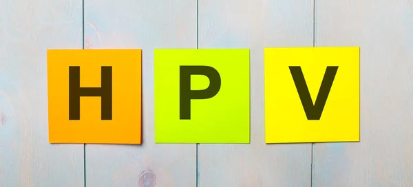 stock image Three colored stickers with the text HPV on a light blue wooden background