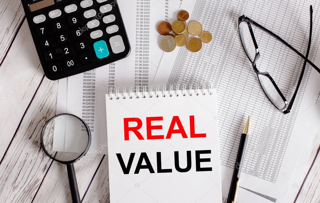 REAL VALUE written in a white notepad near a calculator, cash, glasses, a magnifying glass and a pen. Business concept