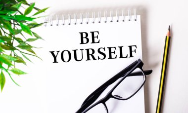 Be You SELF beyaz bir deftere siyah çerçeveli bir kalem ve yeşil bir bitkinin yanında yazılmıştır..